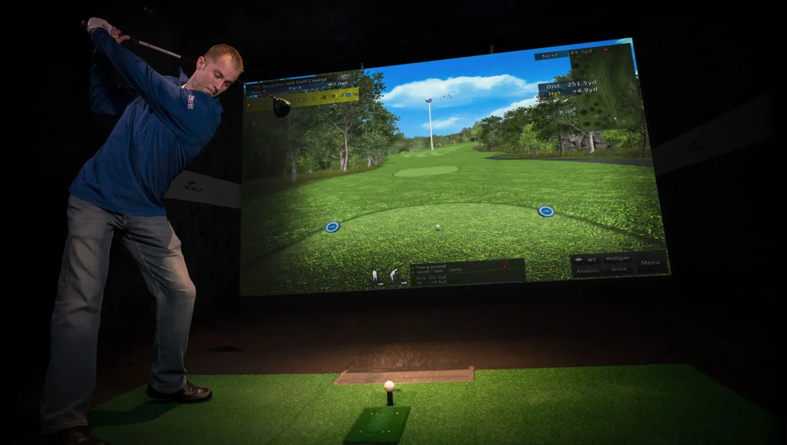 Joueur frappant une balle face à un parcours projeté sur le simulateur de golf